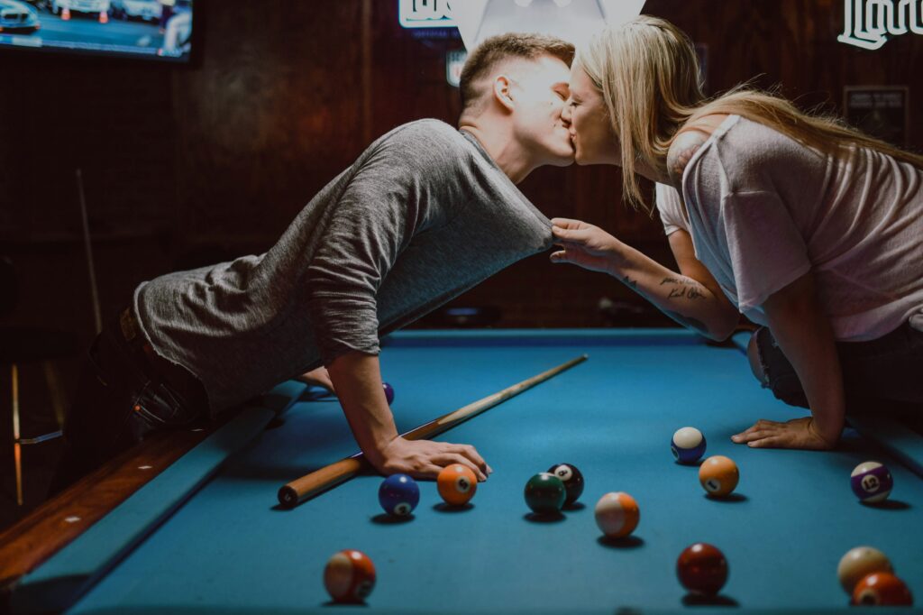 Paar steht sich gegenüber am Billiardtisch und küsst sich