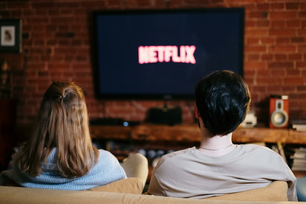 Zwei Menschen sitzen vor einem Flachbildfernsehen der das Netflix-Logo zeigt